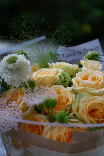 A close-up view of a bouquet featuring pale peach roses with delicate, slightly ruffled petals arranged among white and green filler flowers, including small white pom-pom-like blooms and wispy green 