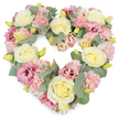 A tender heart-shaped floral wreath is shown against a pristine white background, its pastel colours and lush textures creating a sense of quiet comfort. The heart is densely packed, with no empty spaces, formed by a careful blend of cream and pale yellow roses, soft pink carnations, and richer pink lisianthus flowers. The roses sit proudly as the main anchors, their full, rounded blooms and spiralling centres suggesting purity and enduring love. Pastel pink carnations nestle between them, their frilled, multi-layered petals adding a gentle, almost fluffy softness that softens the outline of the heart. Deeper rose-pink and mauve lisianthus are dotted throughout, their more open, cup-shaped flowers introducing a subtle depth of colour that keeps the eye moving around the arrangement. Silver-green eucalyptus leaves weave through the design, their smooth, rounded leaves and muted tones calming the brighter petals and giving the wreath a harmonious, balanced look. Small, tight yellow-green buds appear in pockets, echoing the freshness of newly opened blooms and the resilience of life. The overall composition is neat and symmetrical, a reflection of the care taken by a Becontree Heath florist who understands how important a floral tribute can be for funerals, cremations, and memorial services in the local area. The palette of creams, blush pinks, dusty rose, and soft green creates a mood of peace and gentle remembrance, like the quiet moments found in nearby Valence Park or along the streets of Becontree Heath after saying farewell. This heart-shaped wreath serves as a poignant symbol of sympathy, gratitude, and unwavering affection for a loved one who will always be remembered.